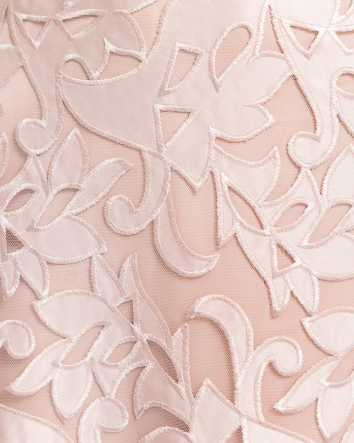 A close-up of an embroidered satin fabric in blush color.