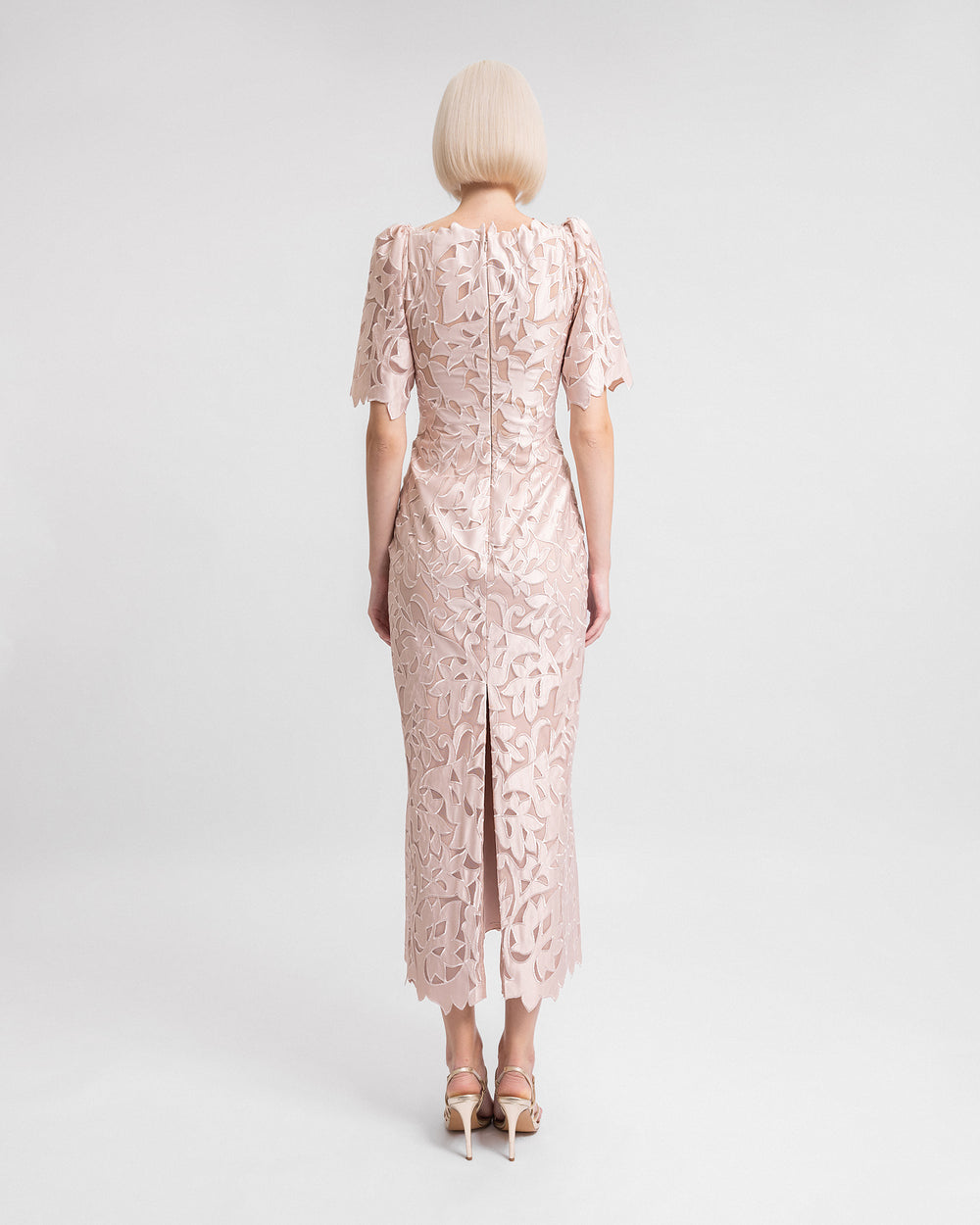 The back of am embroidered satin midi dress in blush color with puffed sleeves and a slit at the back.