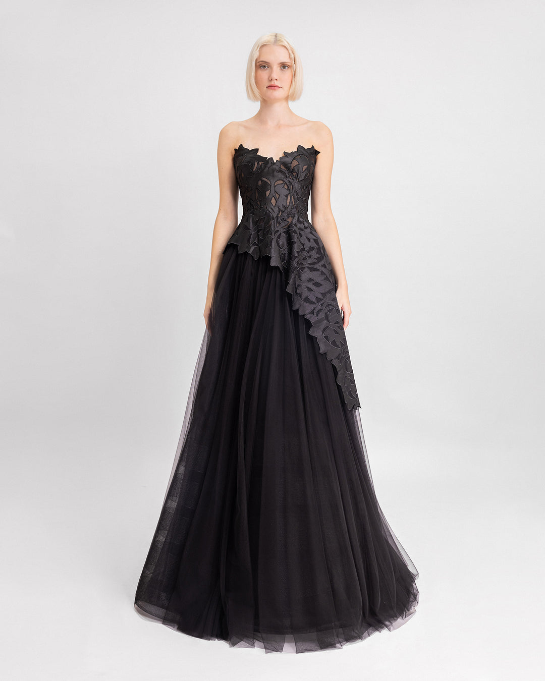 A black evening dress featuring a strapless embroidered satin top with an asymmetrical hemline, paired with a long tulle skirt.