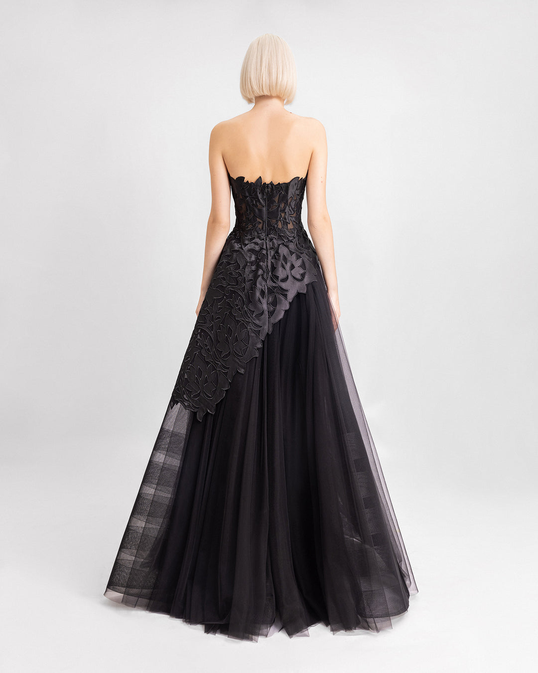 The back of a black evening dress featuring a strapless embroidered satin top with an asymmetrical hemline, paired with a long tulle skirt.