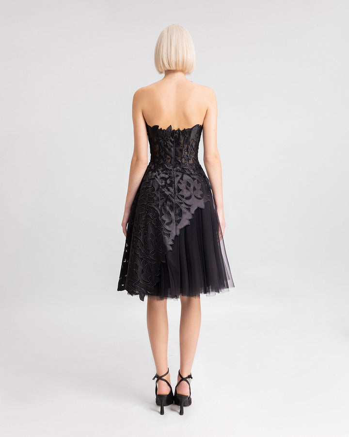 The back of a black strapless evening dress featuring an embroidered satin top with an asymmetrical hemline, paired with a short tulle skirt.