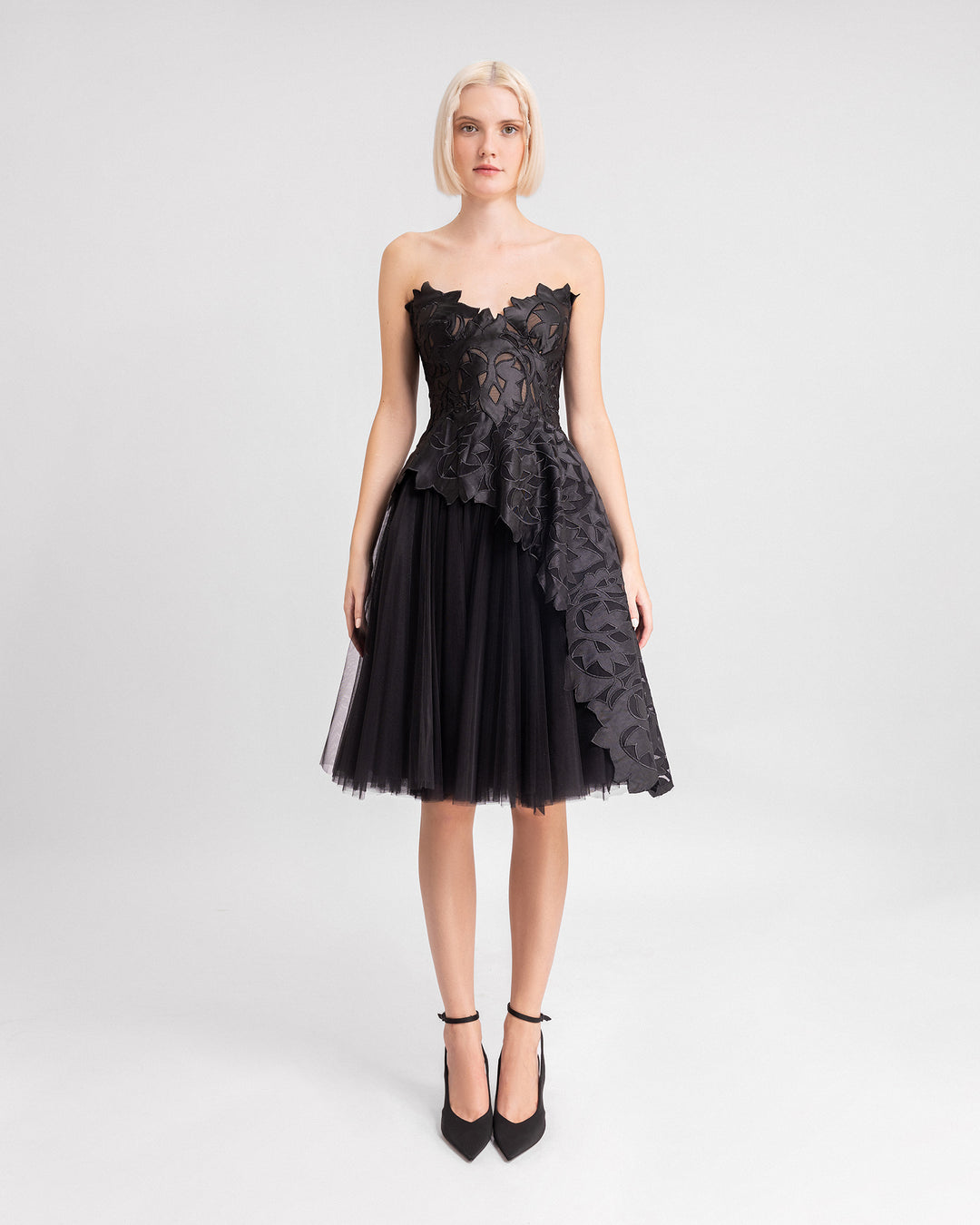 A black strapless evening dress featuring an embroidered satin top with an asymmetrical hemline, paired with a short tulle skirt.