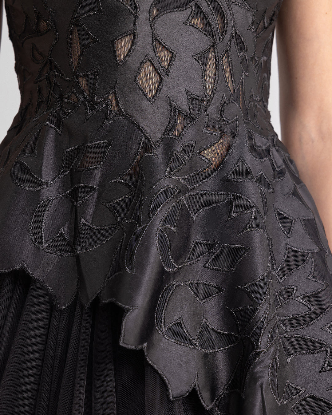 A close-up of a black evening dress featuring an embroidered satin top with an asymmetrical hemline.