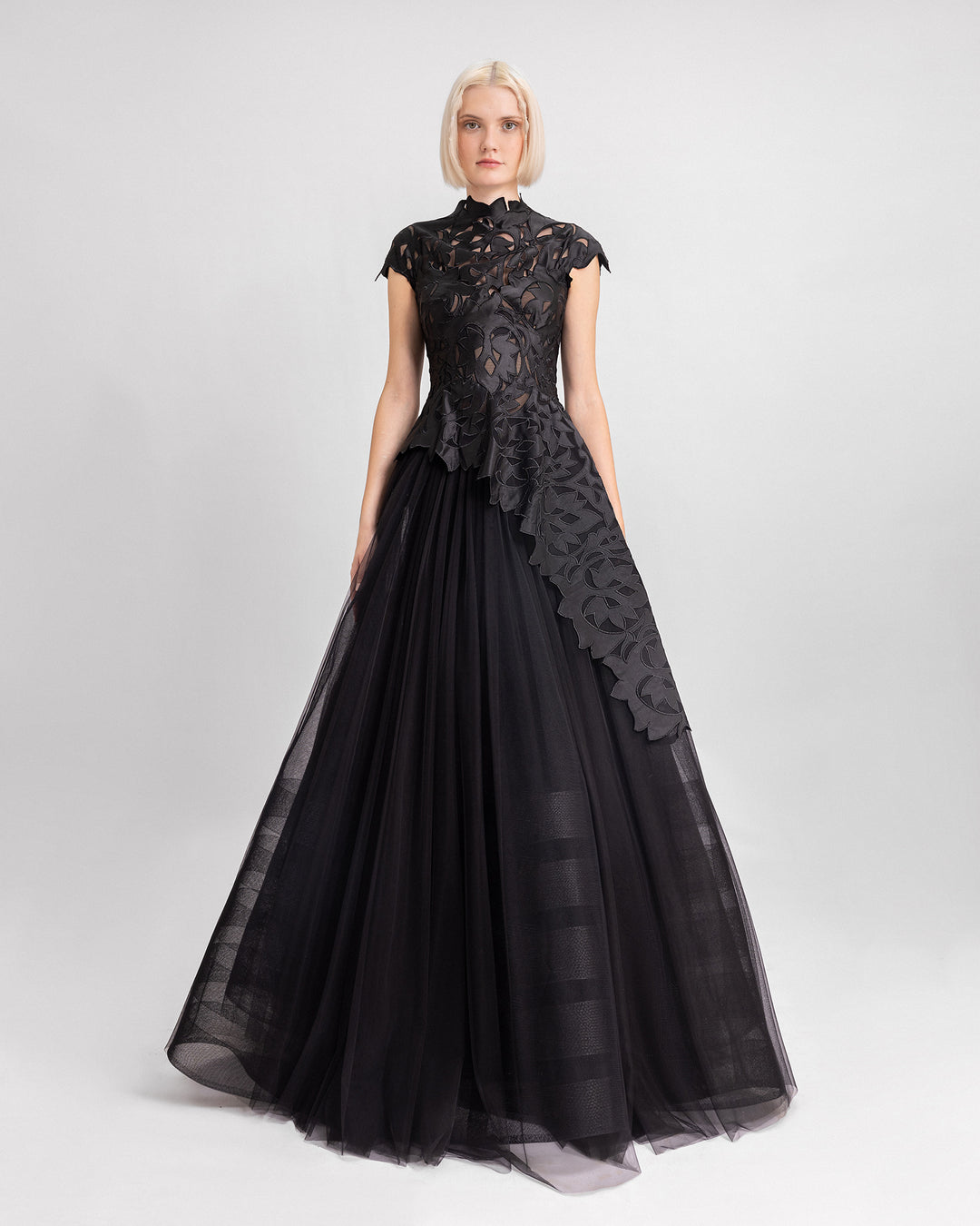 A black evening dress featuring an embroidered satin top with short sleeves and an asymmetrical hemline, paired with a long tulle skirt.