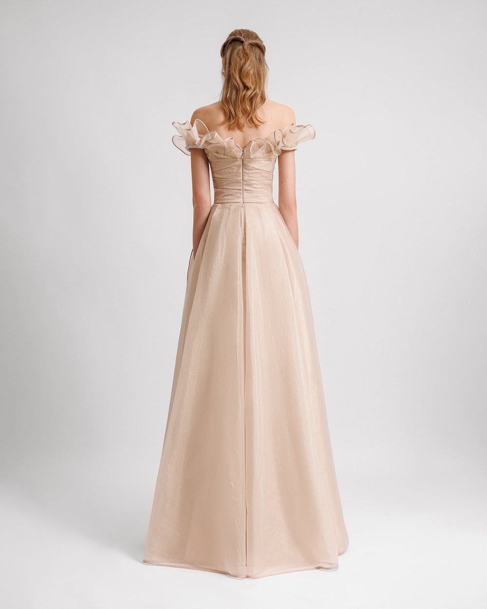 An off-the-shoulders evening dress in champagne color with a layered ruffles neckline and skirt, featuring a draped corset.