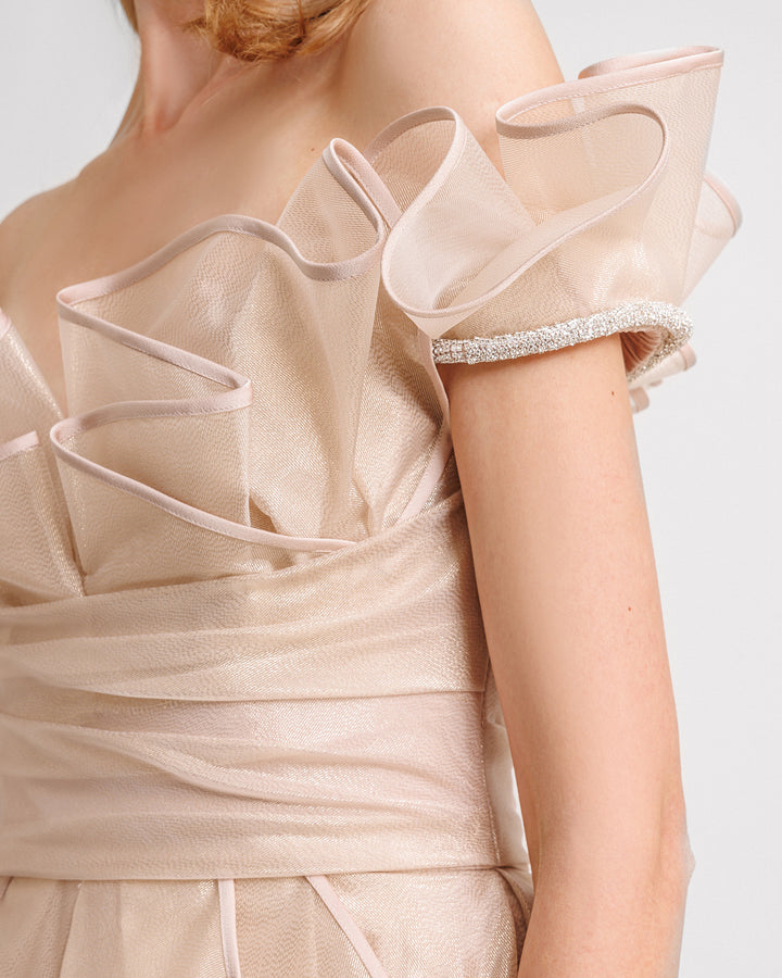 A close-up of an off-the-shoulders evening dress in champagne color with a layered ruffles neckline, beading on the sleeves, and a draped corset.