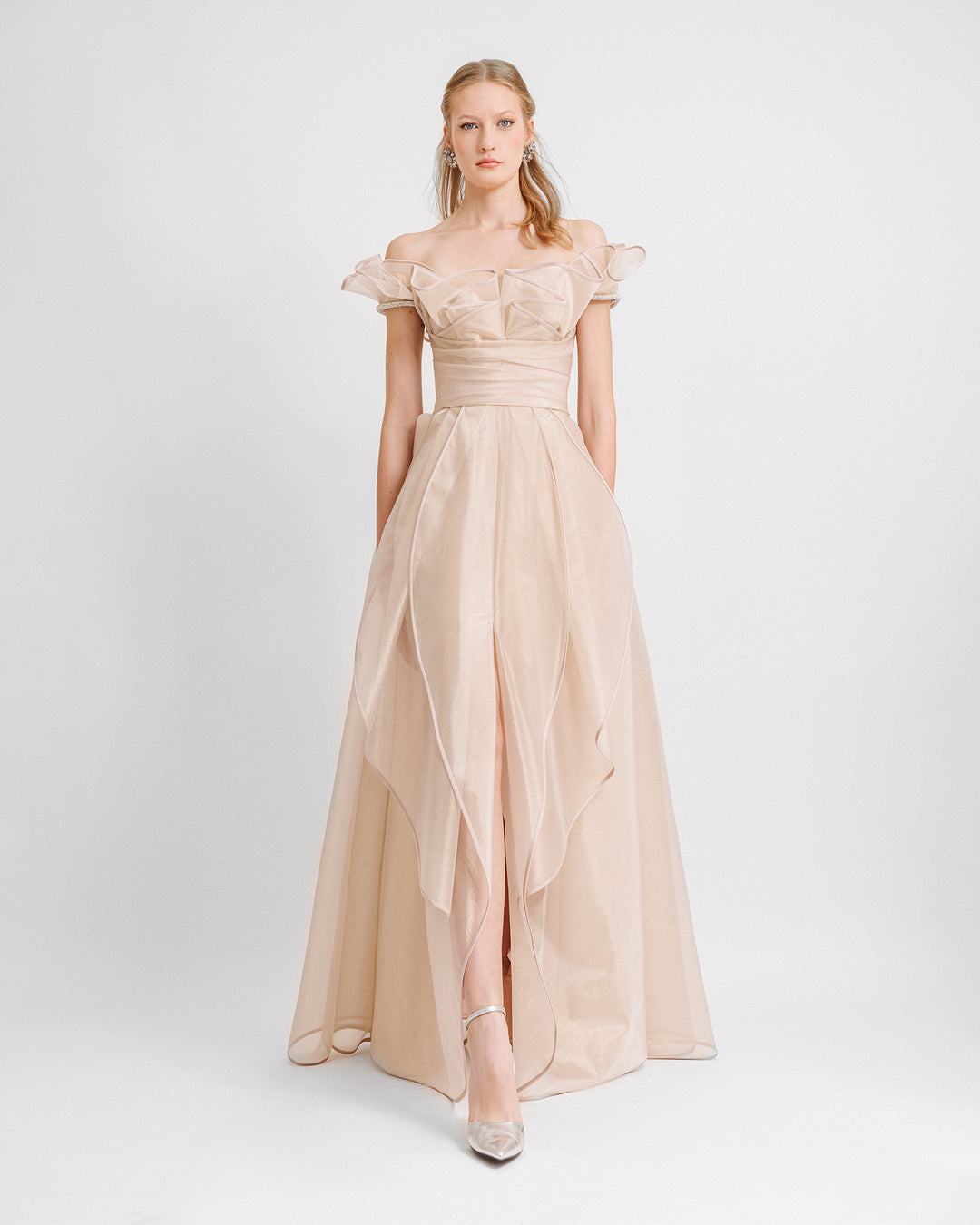 An off-the-shoulders evening dress in champagne color with a layered ruffles neckline and skirt, featuring a draped corset, beadings on the sleeves, and a middle front slit.