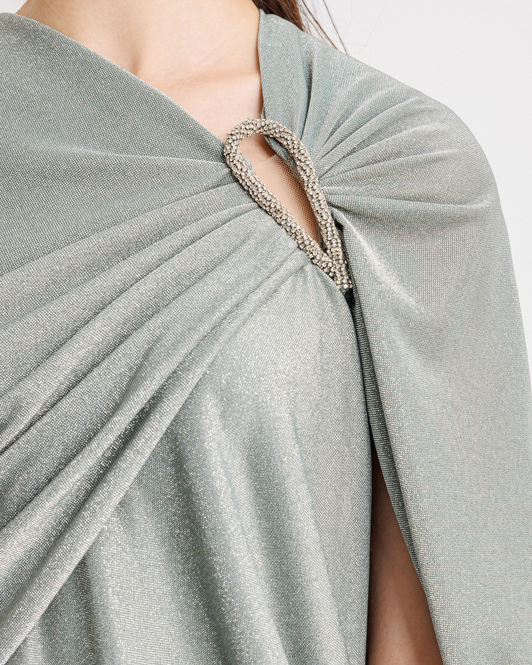 A close-up of an asymmetrical draped evening dress in shiny teal fabric with a beaded cut-out on the shoulder.