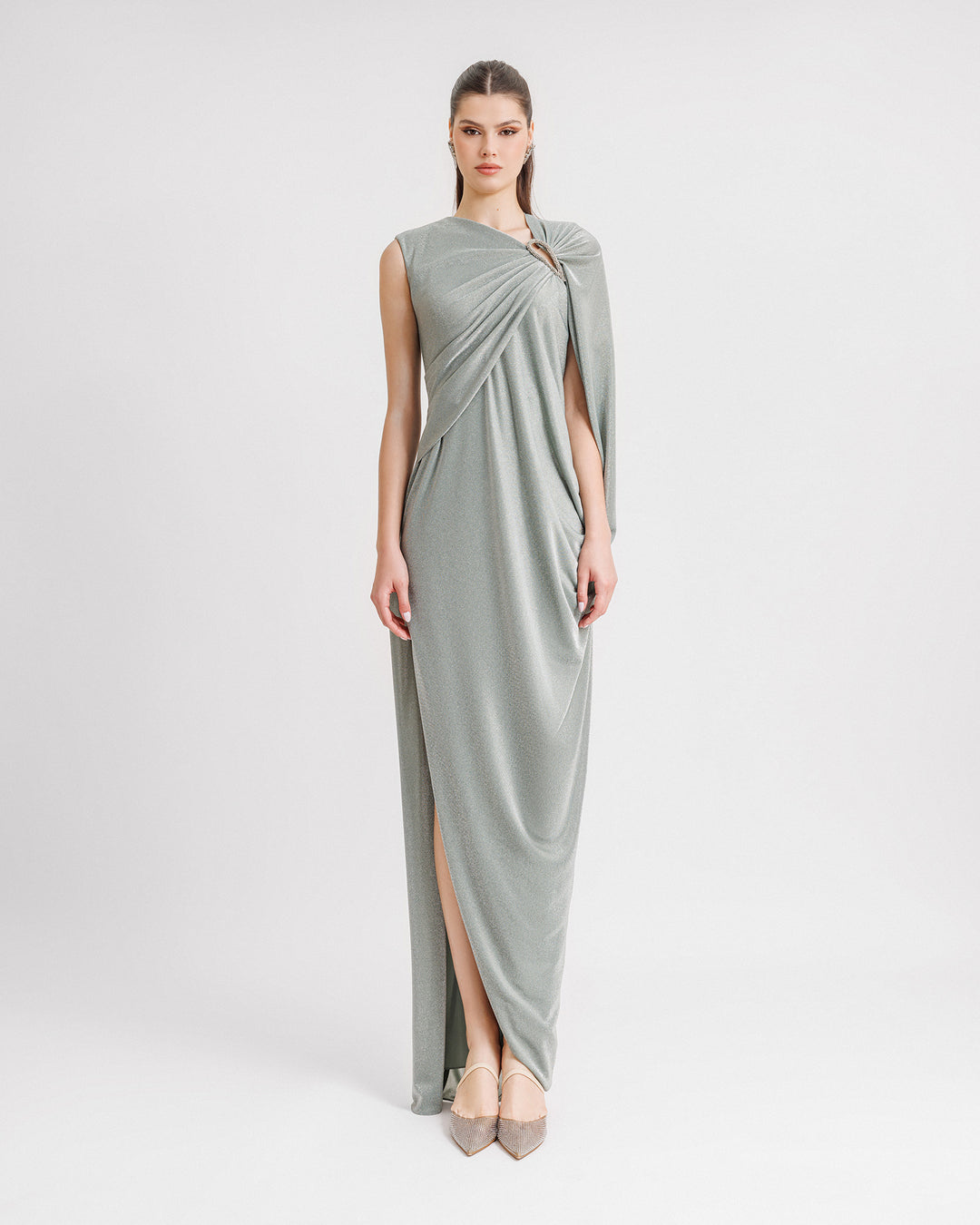 An asymmetrical draped evening dress in shiny teal fabric with a beaded cut-out on the shoulder and a slit on the side.