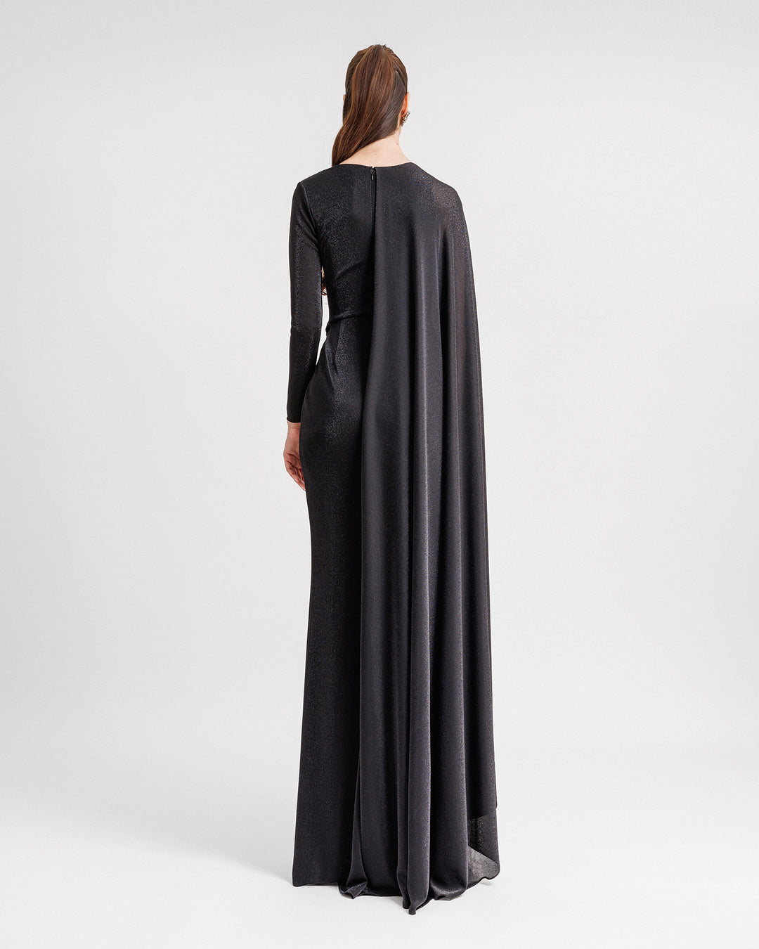 The back of an asymmetrical V-neckline black evening dress with a long sleeve from one side, and a cape-like sleeve on the other side.