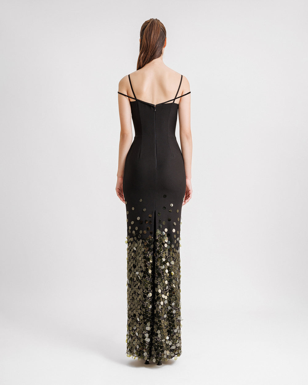 The back of a slim-cut black evening dress with dropped shoulder straps, an open slit at the back, and olive sequins degradation to the hemline.