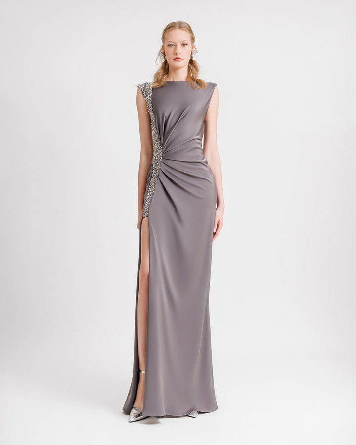 A slim-cut evening dress in smokey grey with draping on the waist and a beaded stripe on one side with an open slit.