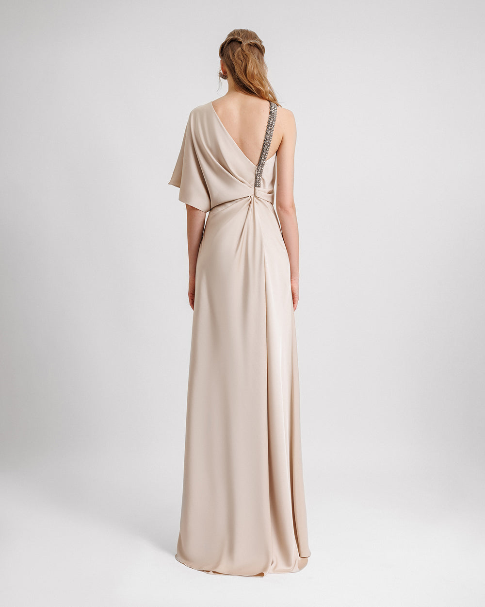 The back of a An asymmetrical neckline champagne dress with draping and a beaded strap at the back.