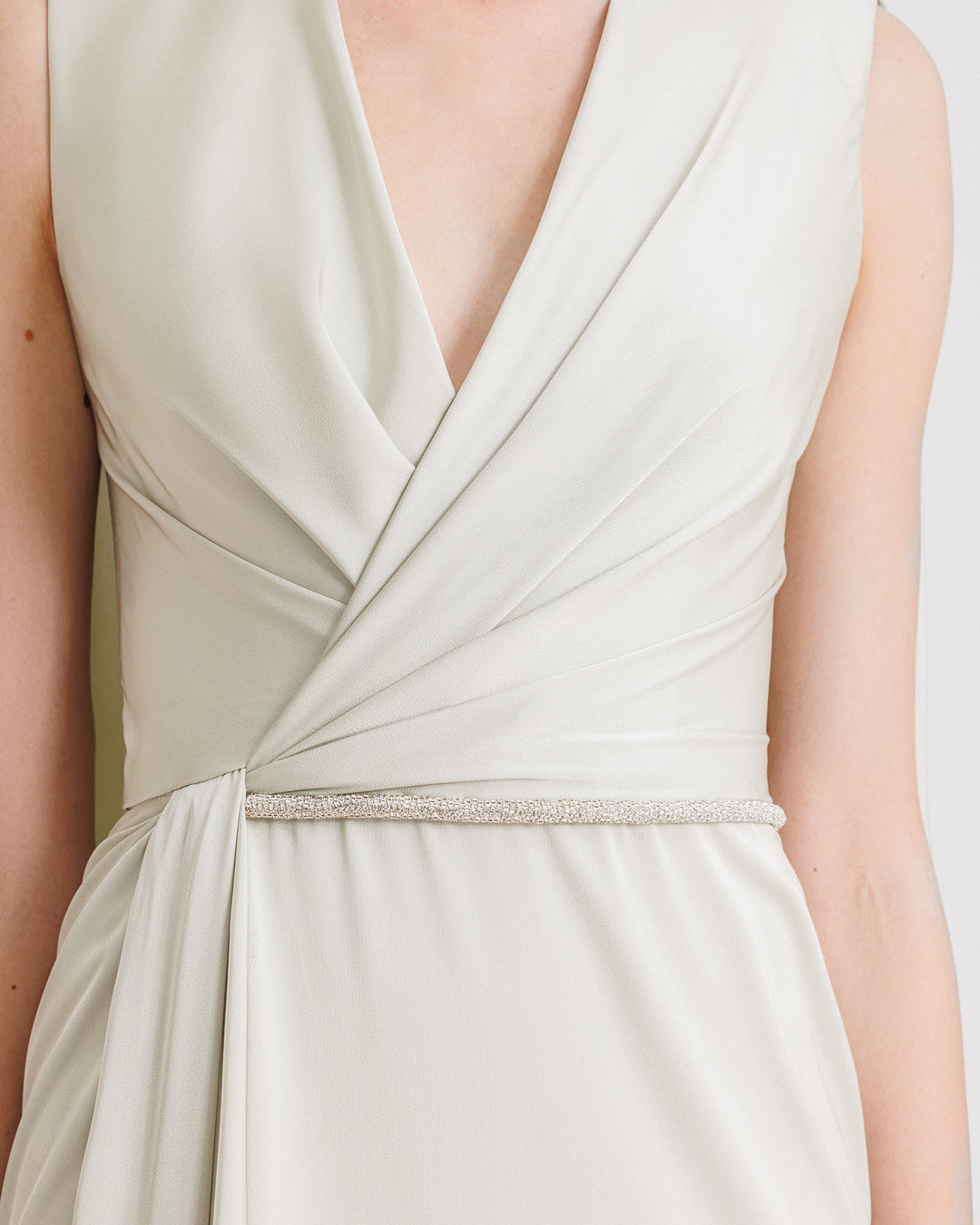 A close-up of V-neckline evening dress in light mint satin fabric with draping and a beaded belt on the waist.