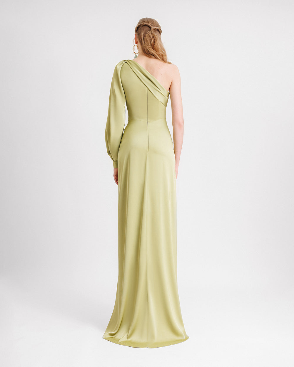 The back of a one-shoulder long sleeve draped evening dress in pistachio satin fabric.