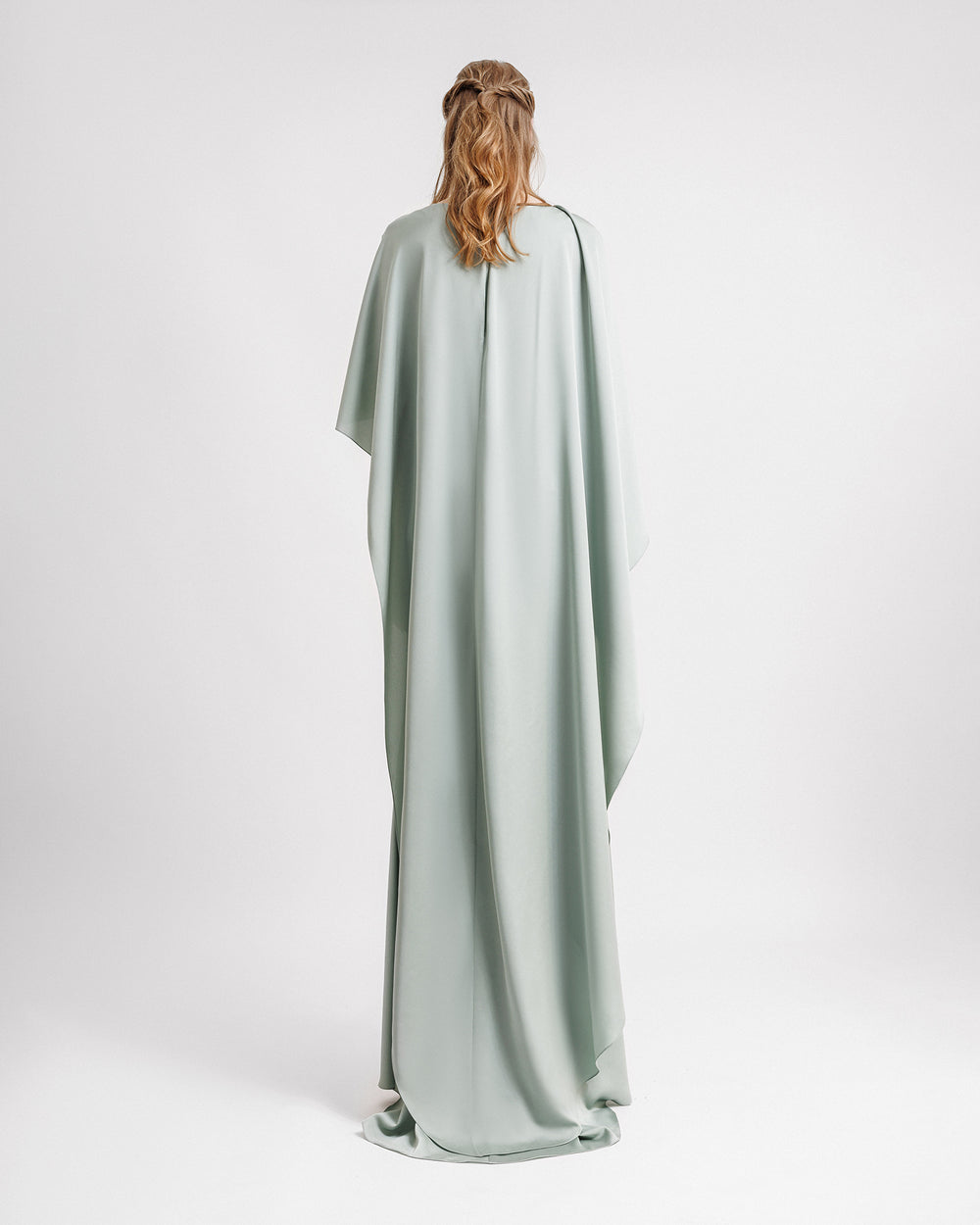 The back of a draped evening dress in teal satin with an asymmetrical cape-like sleeves and back.