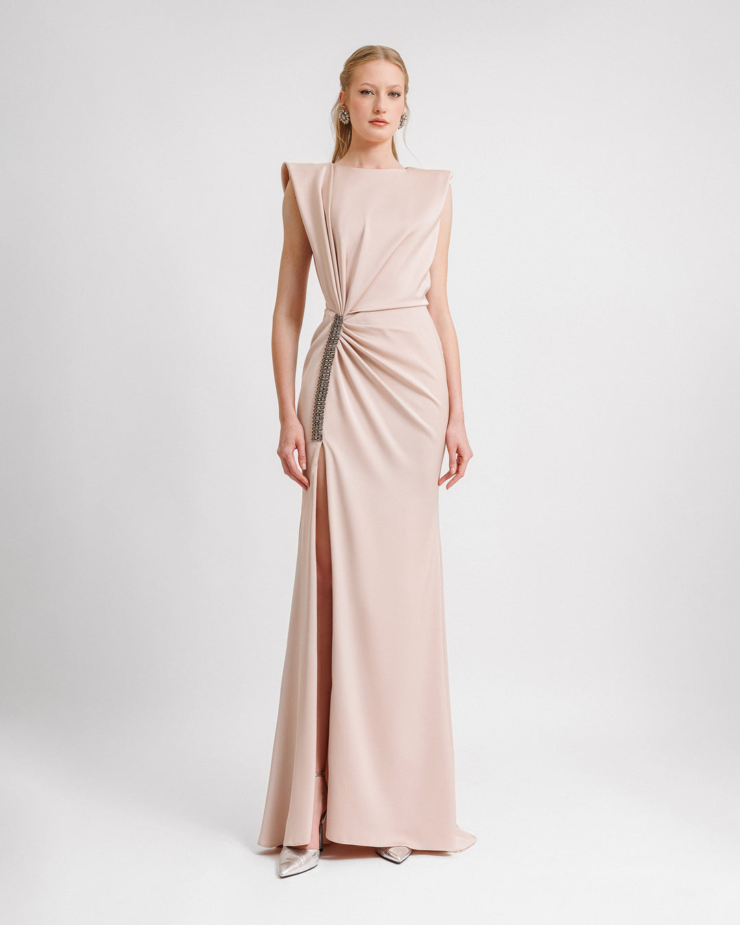 A blush color evening dress with draping on the waist, wide shoulders, and beadings at the side slit.