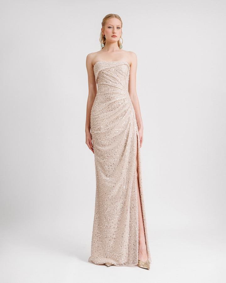 A strapless draped evening dress in champagne beaded tulle with an asymmetrical fold-over neckline and a slit on the side.