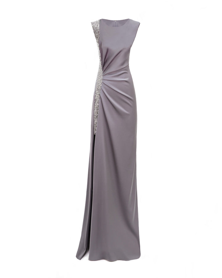 A slim-cut evening dress in smokey grey with draping on the waist and a beaded stripe on one side with an open slit.