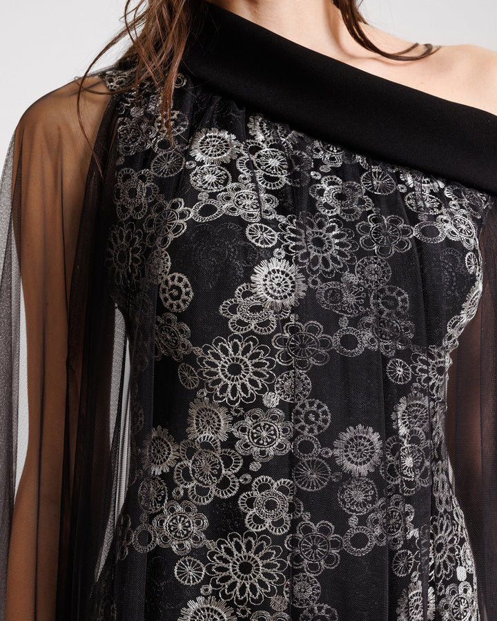 A close-up of an embroidered asymmetrical neckline black evening dress with a tulle overlay.