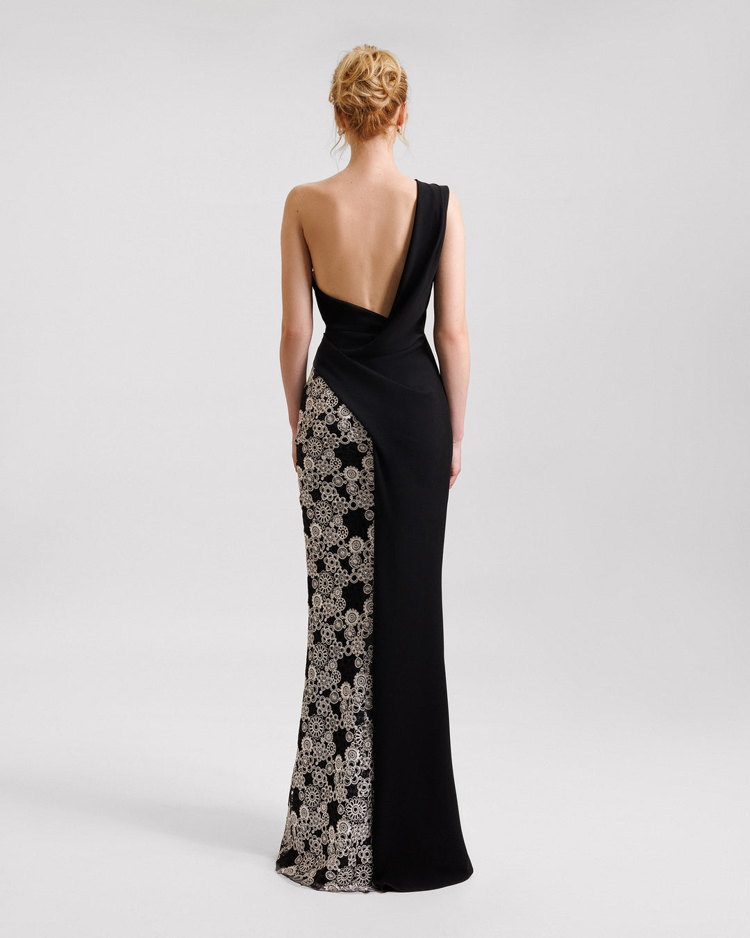 The back of a one-shoulder black evening dress with draping and a slit on one side, and embroidery on the other.