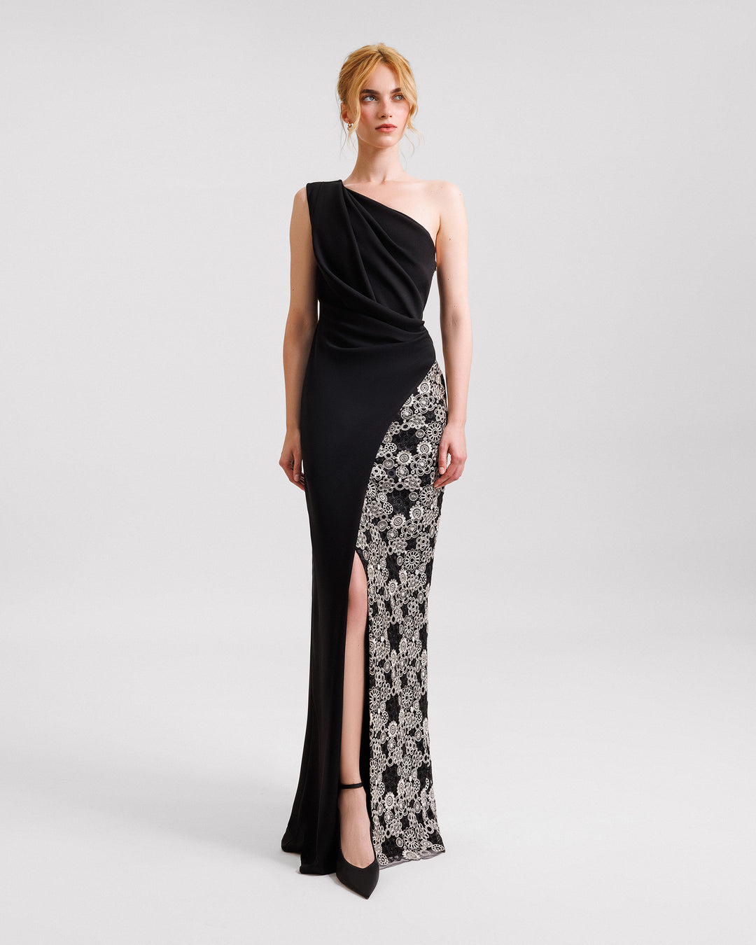 A one-shoulder black evening dress with draping and a slit on one side, and embroidery on the other.