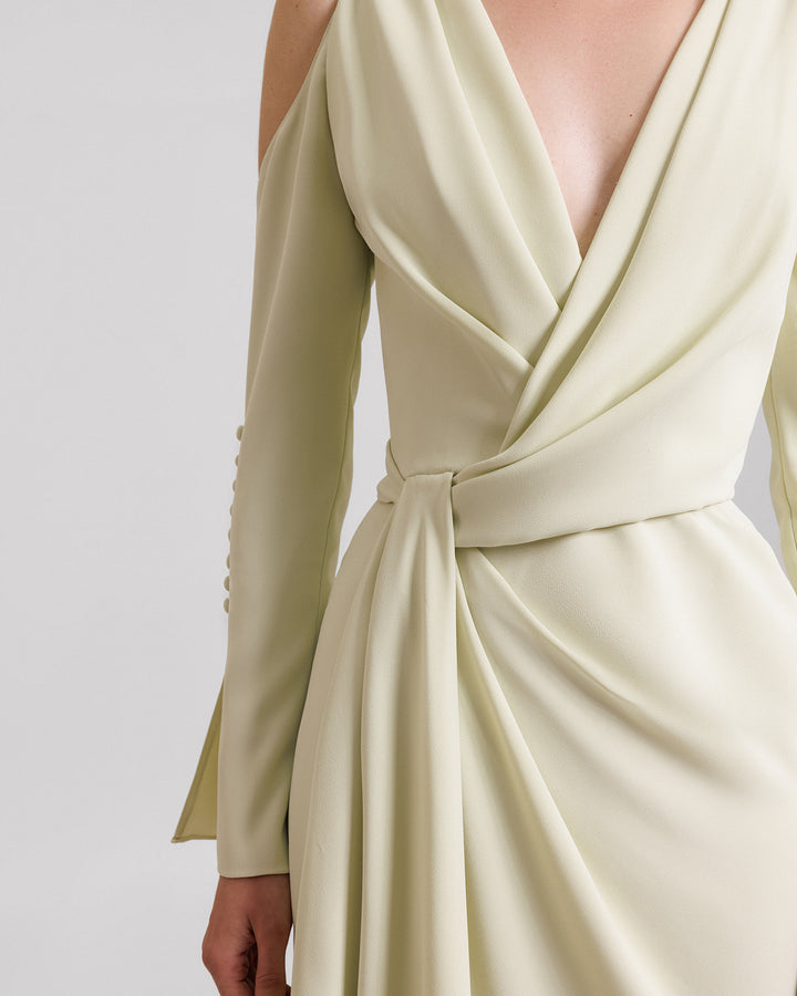 A close-up of a v-neckline evening dress in pale lime color with draping on the waistline, cut-outs on the shoulders, and buttons on the sleeves.