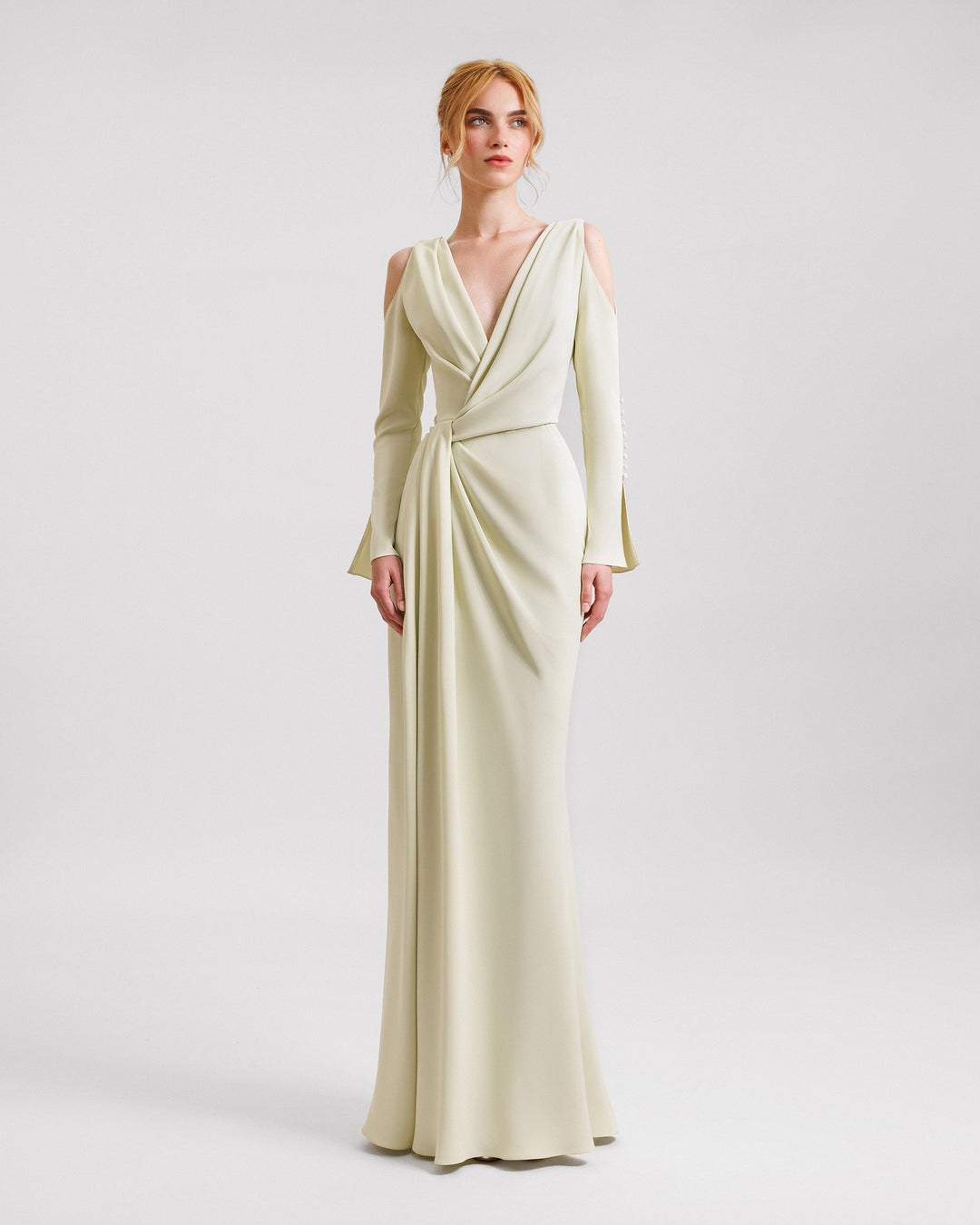 A v-neckline evening dress in pale lime color with draping on the waistline, cut-outs on the shoulders, and buttons on the sleeves.