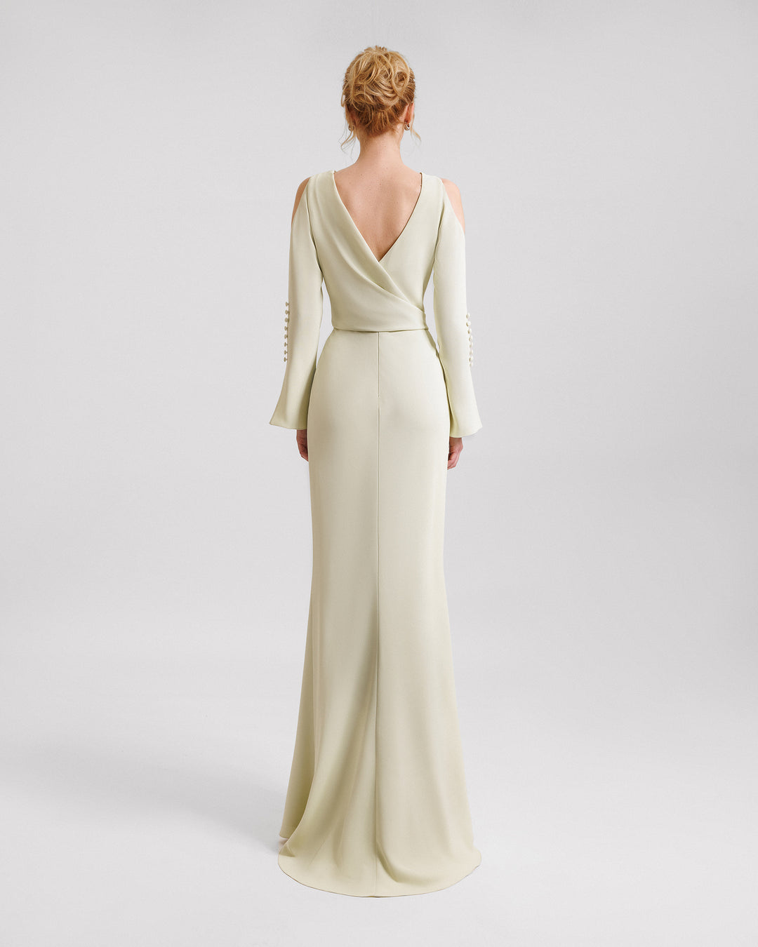 The back of a pale lime evening dress with draping on the waistline, cut-outs on the shoulders, and buttons on the sleeves.