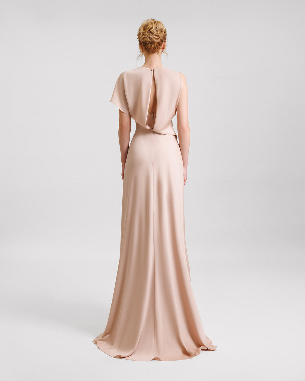 The back of a long draped evening dress in beige color featuring a cut-out at the back.