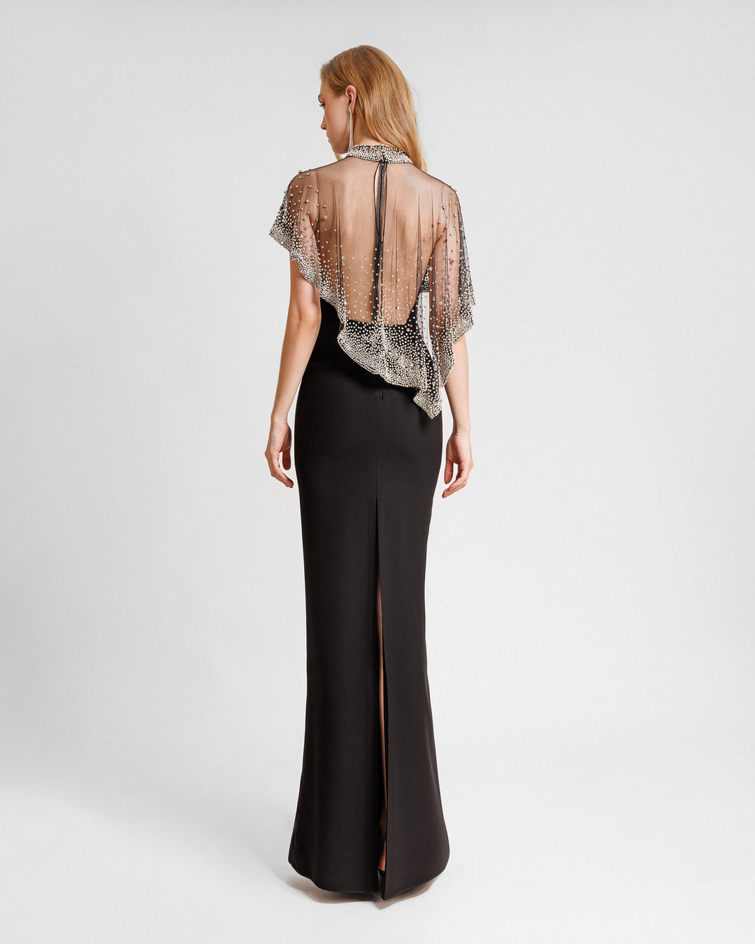 An open back straight-cut black evening dress with an asymmetrical beaded tulle overlay, low back, and a slit at the back.