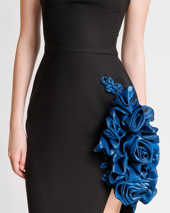 A close-up of a slim-cut black evening dress featuring petrol floral draping and a slit on the side.