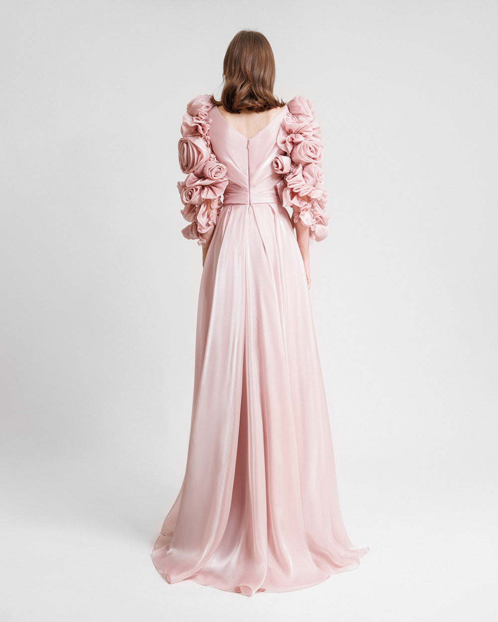 The back of a flared pink evening dress in pink color featuring draping on the waist and full floral sleeves.