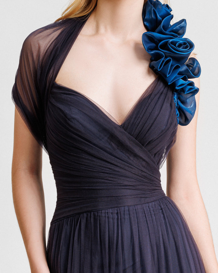 A close-up of an asymmetrical neckline flared evening dress in navy draped tulle with floral draping on the shoulder.