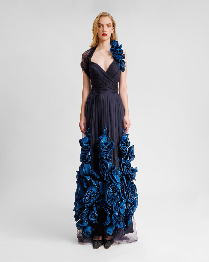 An asymmetrical neckline flared evening dress in navy draped tulle with floral draping on the shoulder and hemline.