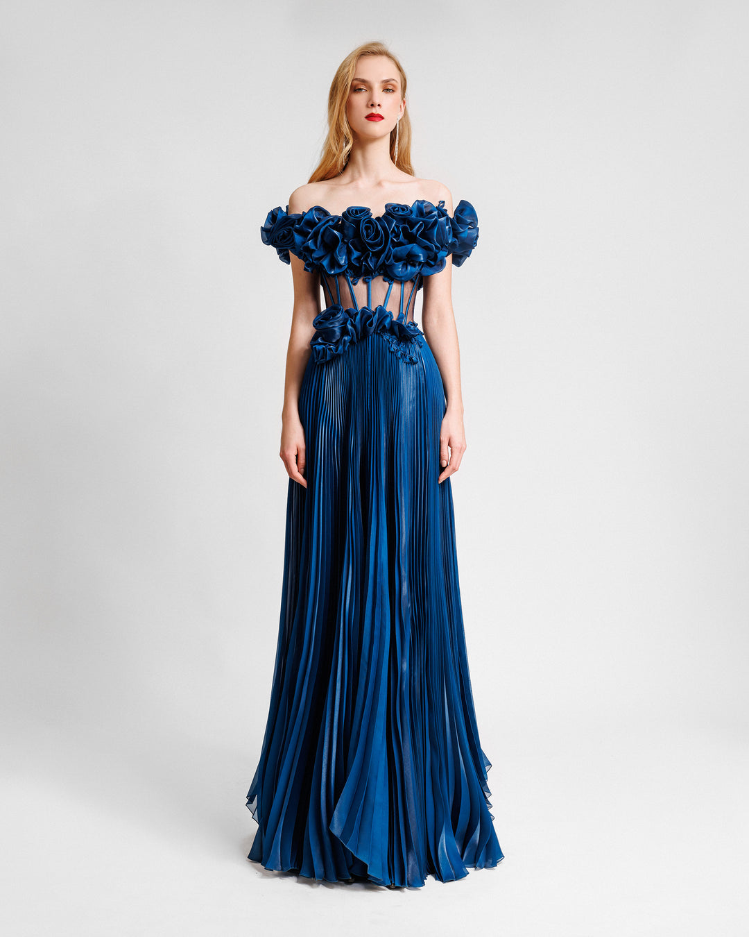 A petrol evening dress with off-the-shoulders floral draping, featuring a see though corset and a pleated skirt.