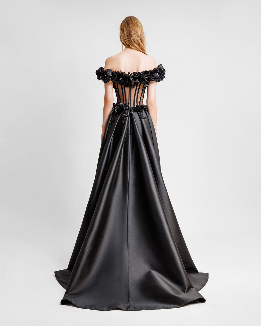 The back of a black evening dress featuring a floral draping off-the-shoulders, a see-through corset, and a train at the back.