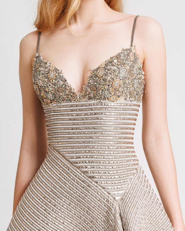 A close-up of a beaded bust evening dress in champagne color featuring an asymmetrical waist cut.