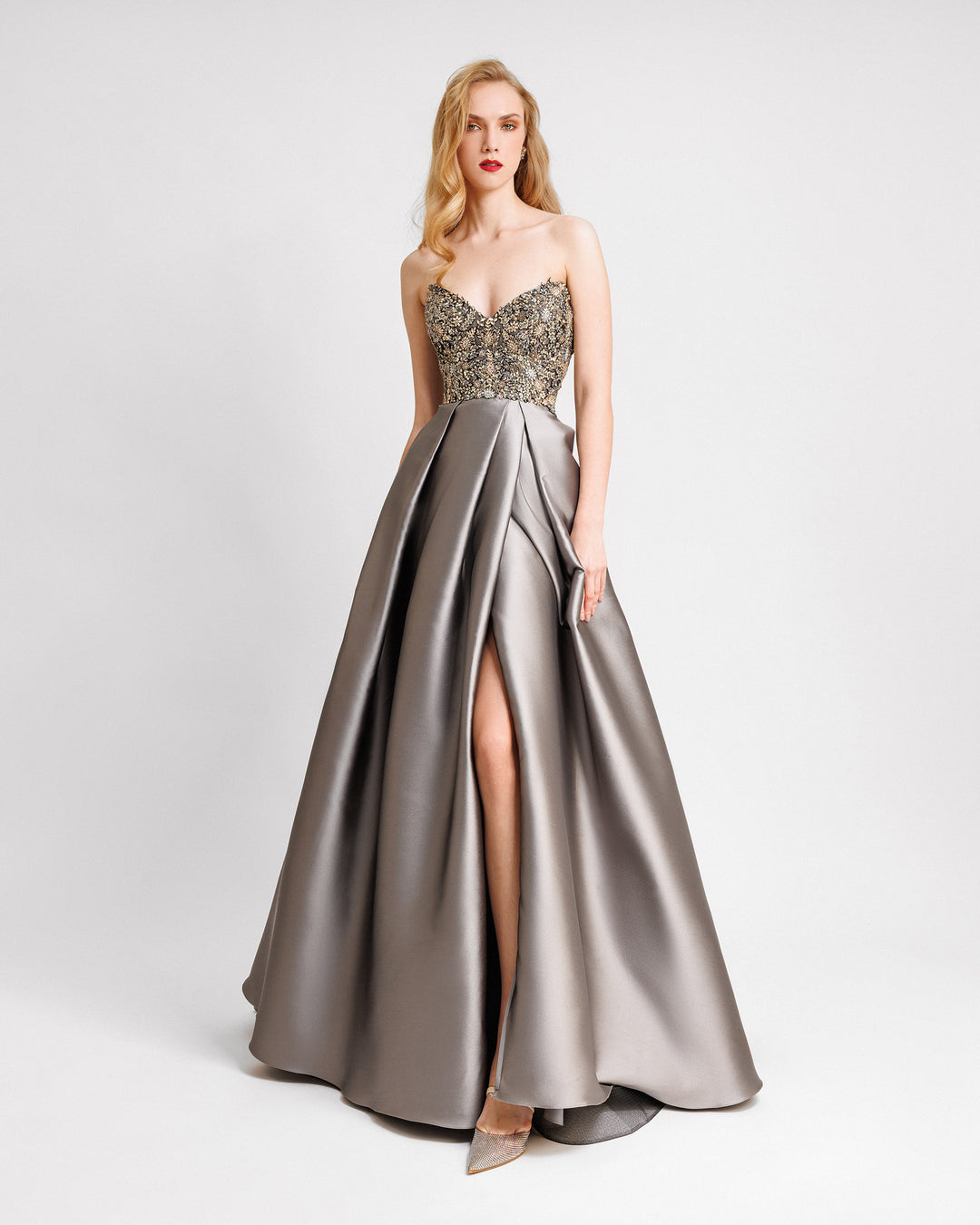 A strapless beaded corset evening dress with a draped full skirt featuring a slit on the side.