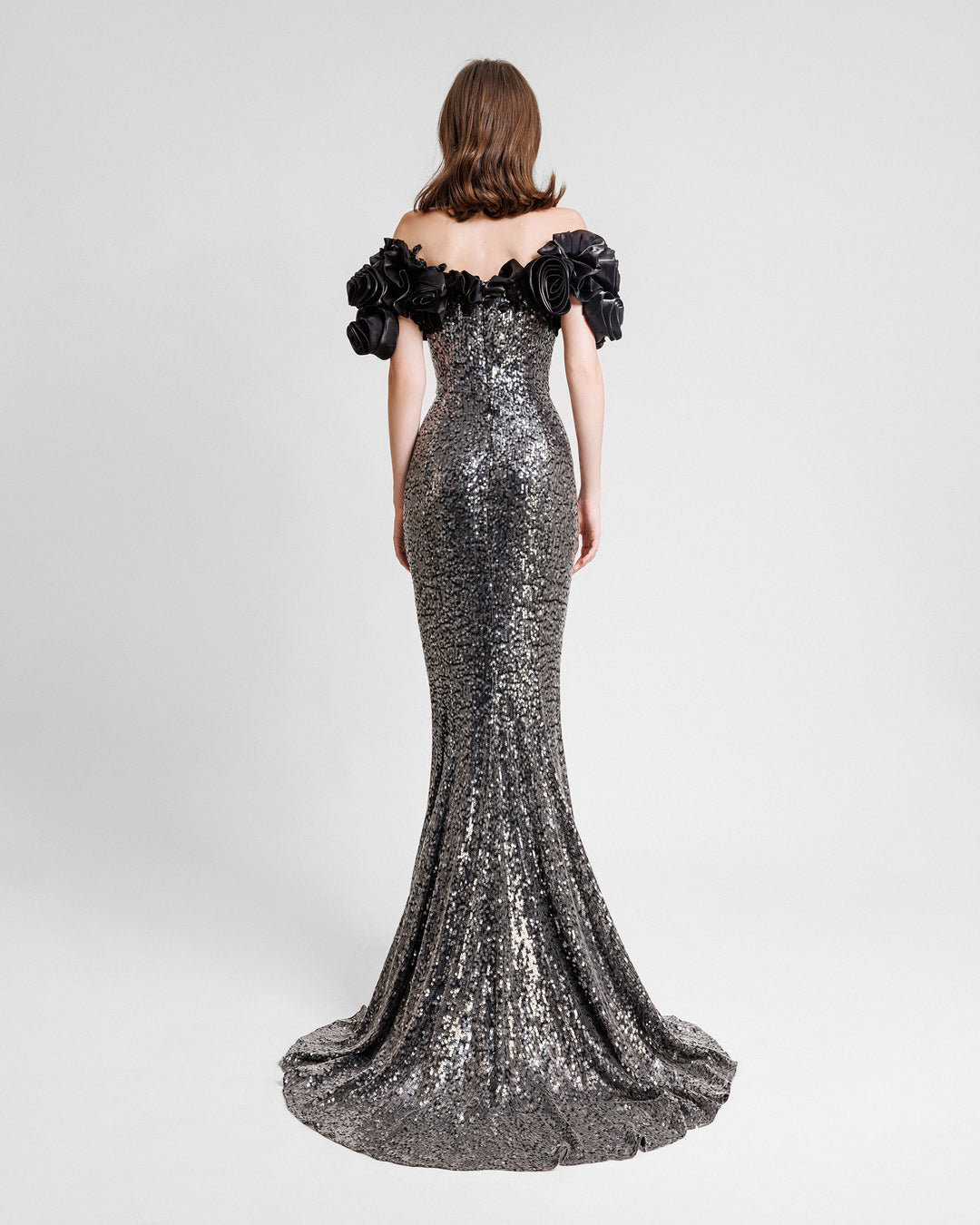 The back of a fully sequined slim-cut evening dress featuring black floral draping off-the-shoulders.