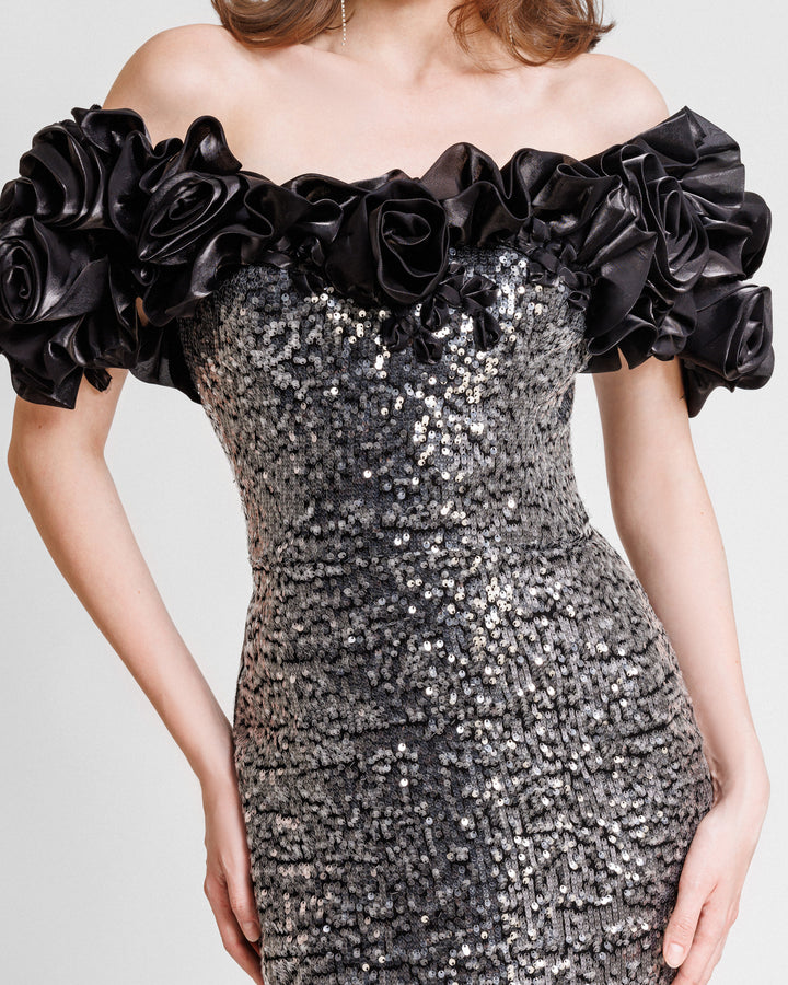 A close-up of a fully sequined slim-cut evening dress featuring black floral draping off-the-shoulders.