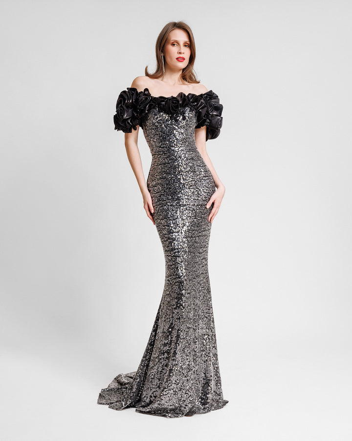 A fully sequined slim-cut evening dress featuring black floral draping off-the-shoulders.