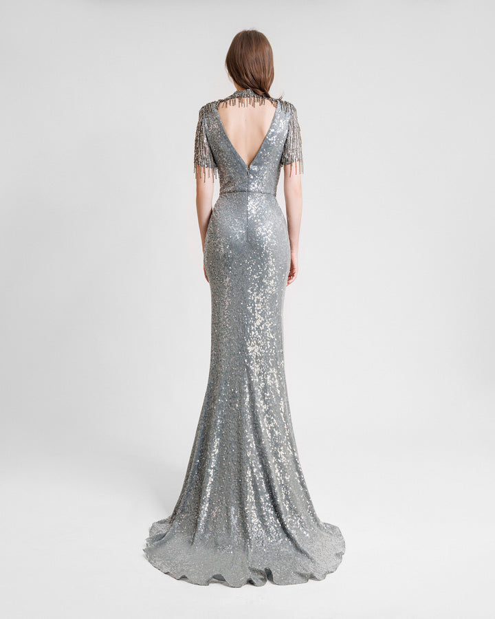 The back of a grey evening dress featuring a deep v-shape back cut out, embroidered sequins neck and sleeves, and a slit at the front.