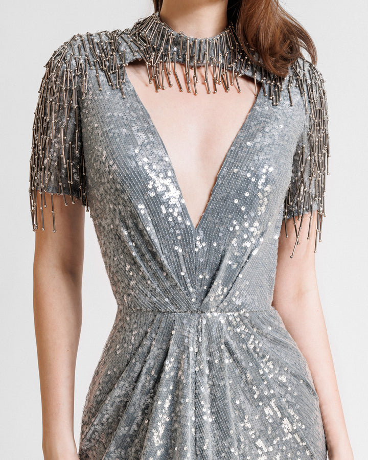 A close-up of a grey evening dress featuring a deep v-neckline cut out, embroidered sequins neck and sleeves, and a slit at the front.