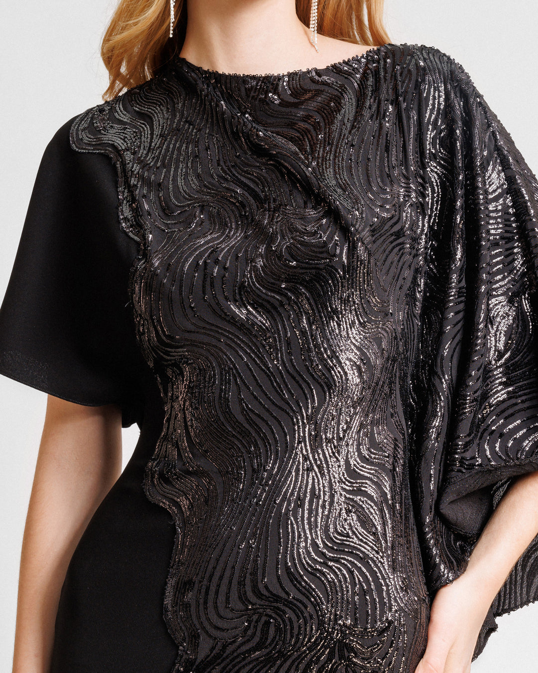 A close-up of an asymmetrical sleeves, embroidered sequins slim-cut black dress with a black crepe side.