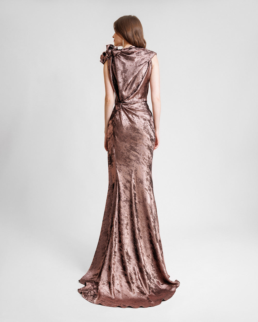 The back of a long draped evening dress in metallic pink with flowers on the shoulder and draping on the waist.