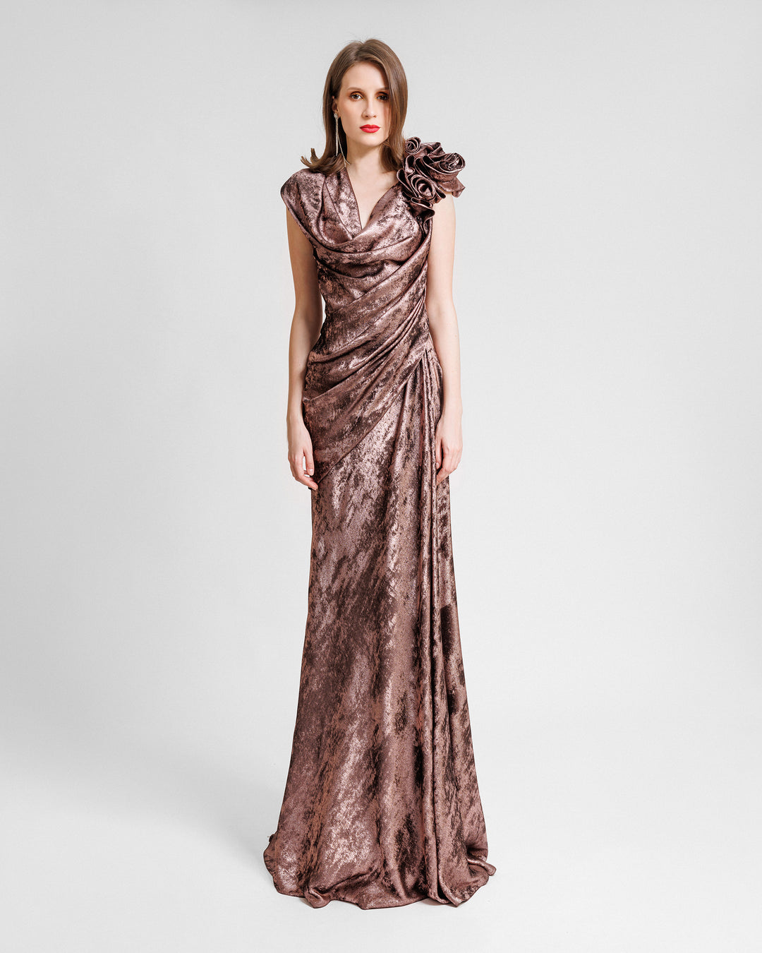 A draped long evening dress in metallic pink with a cowl neckline and draped flowers on the shoulder.