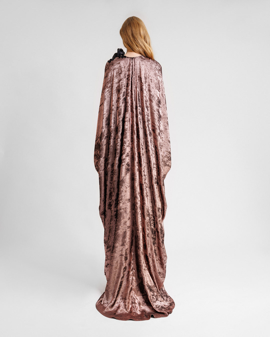 The back of a loose-cut kaftan dress in metallic pink with floral draping on the shoulder.