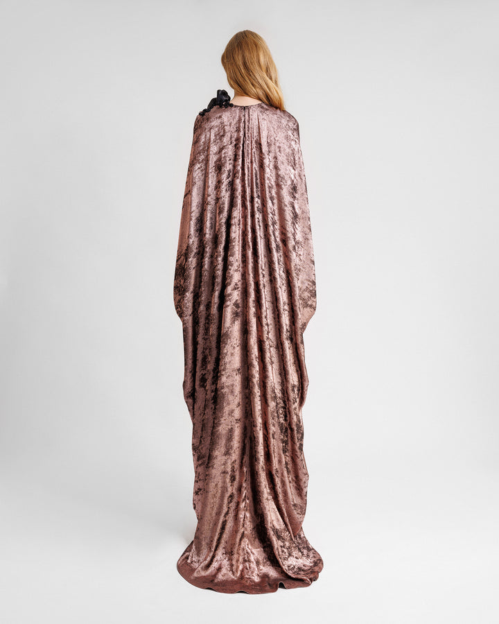 The back of a loose-cut kaftan dress in metallic pink with floral draping on the shoulder.