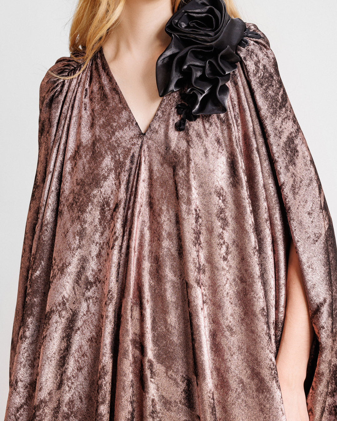 A close-up of a v-neckline loose-cut kaftan dress in metallic pink with floral draping on the shoulder.